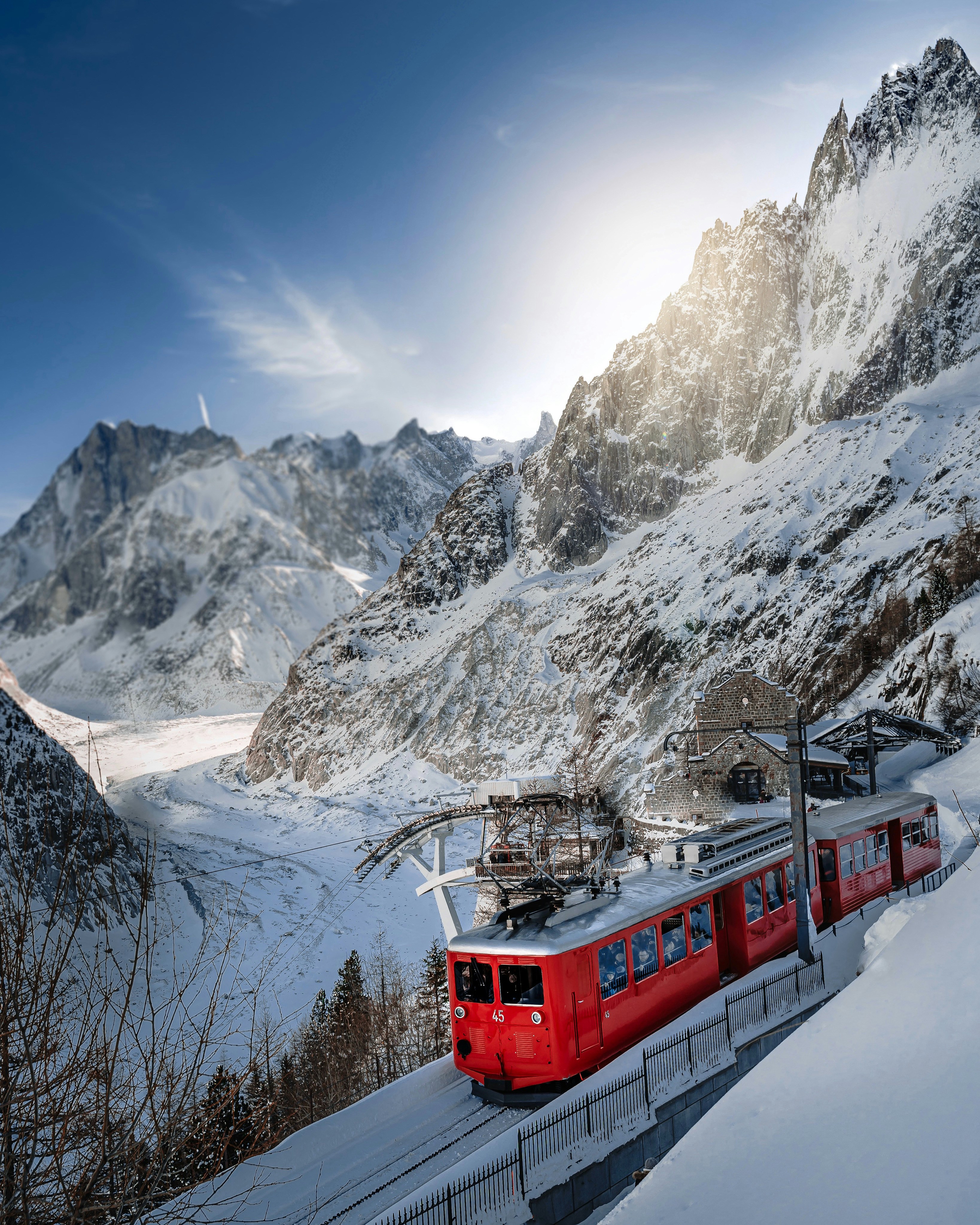 Red mountain railway train climbing through snowy alpine peaks in the French Alps during winter